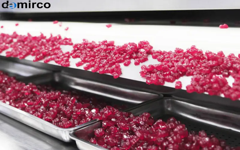 نمایی نزدیک از پاستیل‌های بسته‌بندی شده در انواع مختلف، از جمله سلفون، ظروف پلاستیکی و پاکت‌های ایستاده. تعدادی ماشین‌آلات بسته‌بندی صنعتی نیز در پس‌زمینه دیده می‌شوند که بر فرآیند اتوماسیون تأکید دارند