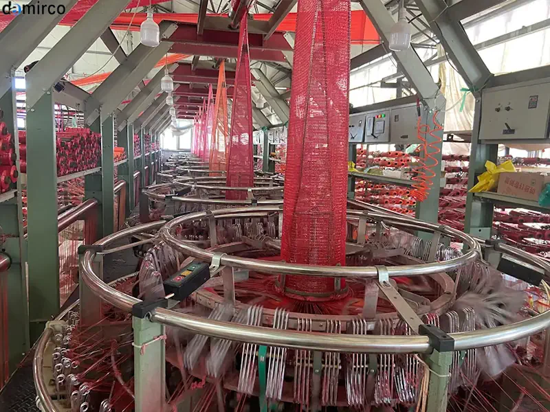 دستگاه توری پیاز در حال تولید توری پلاستیکی نارنجی رنگ برای بسته‌بندی پیاز در یک کارخانه صنعتی.