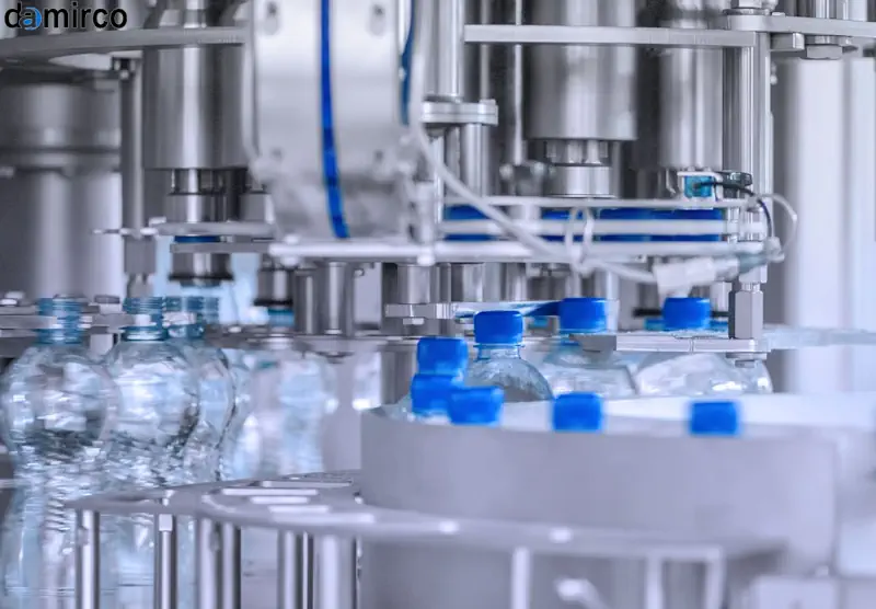 یک دستگاه درب بند بطری پت در خط تولید در حال بستن درب‌های آبی رنگ بر روی بطری‌های شفاف نوشیدنی