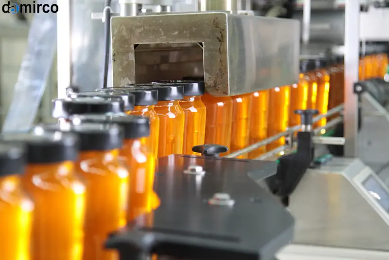 دستگاه درب بند اتوماتیک در حال بستن درب شیشه های مربا در یک خط تولید صنعتی