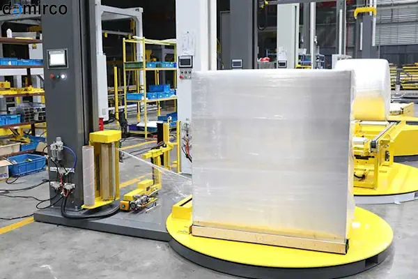 یک دستگاه استرچ پالت اتوماتیک پیشرفته در حال بسته‌بندی یک پالت پر از جعبه در یک انبار مدرن