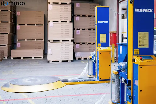 یک دستگاه استرچ پالت صنعتی در حال بسته‌بندی پالت پر از کارتن در انبار