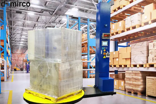 یک دستگاه استرچ پالت در حال بسته‌بندی یک پالت پر از کارتن در یک انبار صنعتی