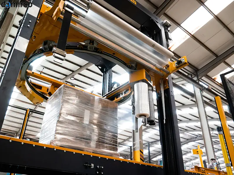 یک دستگاه استرچ پالت تمام اتوماتیک در حال بسته‌بندی پالت در یک کارخانه در کنار یک دستگاه نیمه اتوماتیک