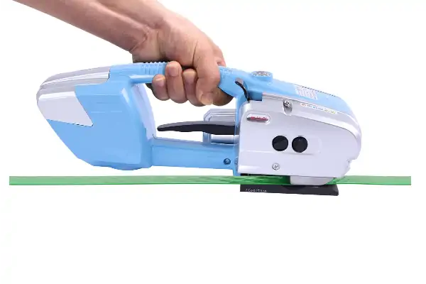 یک کارگر در حال استفاده از دستگاه تسمه کش شارژی برای بسته‌بندی یک پالت صنعتی.