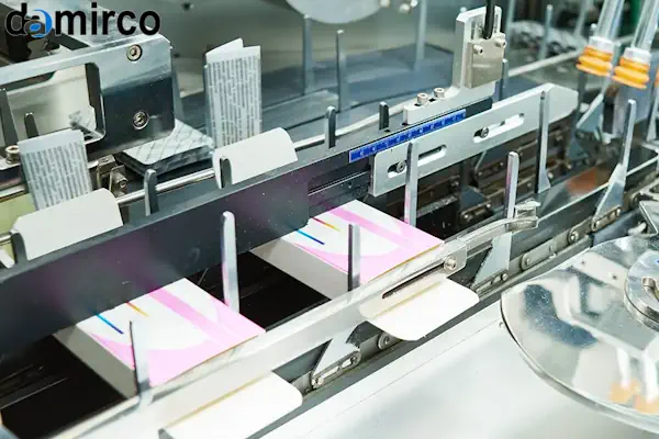 نمای نزدیک از نازل یک دستگاه چسب هات ملت صنعتی در حال اعمال چسب بر روی جعبه مقوایی