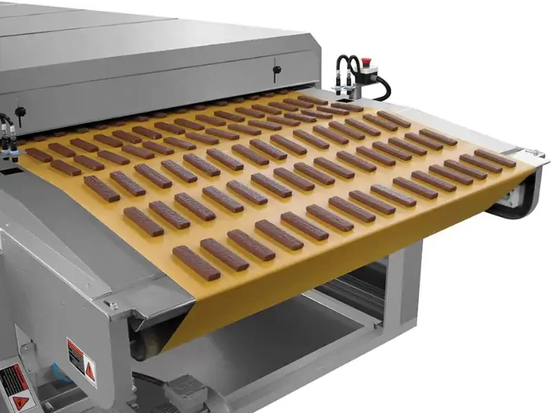 نمای داخلی یک تونل سرد کن شکلات صنعتی با شکلات‌های در حال حرکت روی نوار نقاله