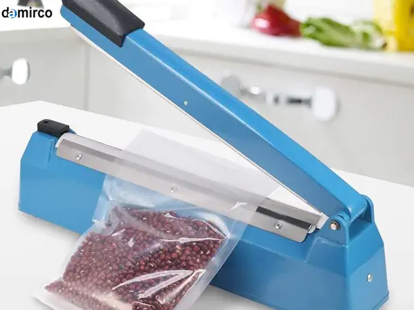 یک دستگاه دوخت پلاستیک دستی آبی رنگ روی میز کار در حال پلمپ کردن یک بسته پلاستیکی