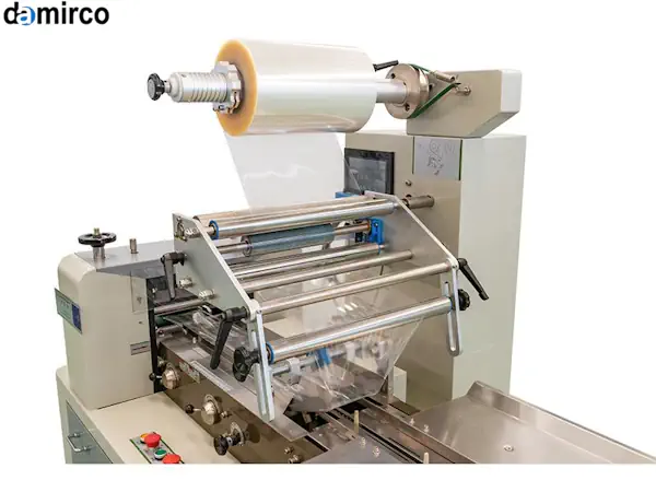 تصویر یک دستگاه بسته بندی افقی پیلوپک در حال بسته بندی بیسکوییت در یک خط تولید صنعتی