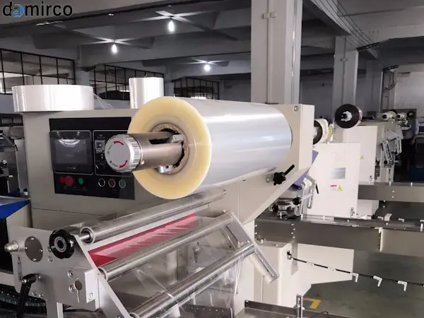 یک دستگاه بسته بندی پیلو پک صنعتی در حال بسته بندی بیسکوییت با سلفون شفاف