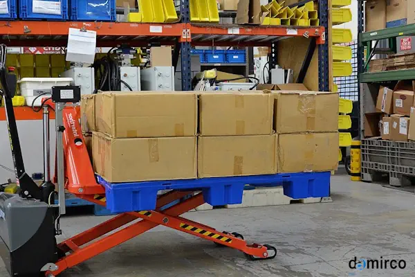 یک دستگاه جک پالت قیچی نارنجی رنگ در حال بلند کردن پالت چوبی در یک انبار صنعتی