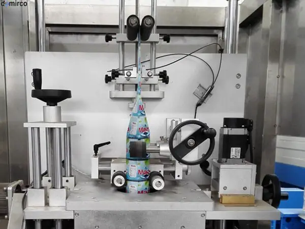 یک دستگاه لیبل زن حرارتی شیرینگ در حال لیبل زدن بطری های شامپو در یک خط تولید صنعتی