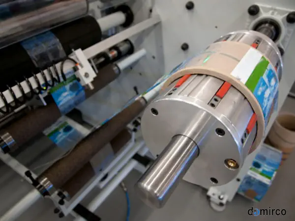 دستگاه لیبل شیرینگ تمام اتوماتیک در حال لیبل‌زنی بطری‌های نوشیدنی روی نوار نقاله در یک کارخانه مدرن