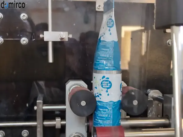 تصویر یک دستگاه شیرینگ لیبل غلاف زن صنعتی در حال لیبل زدن بطری های نوشیدنی