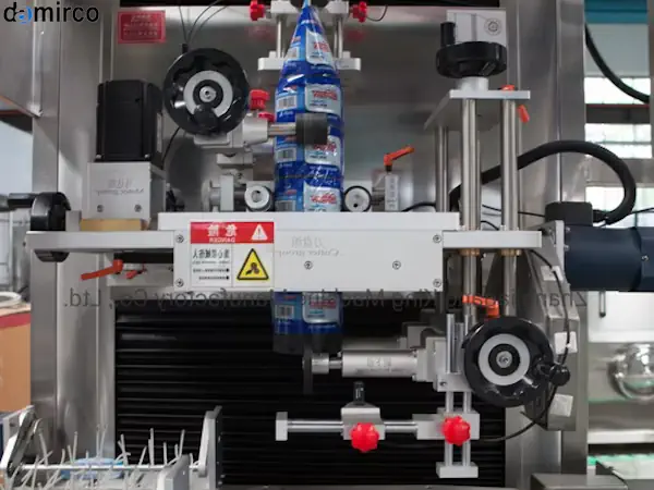 یک دستگاه لیبل شیرینگ در حال الصاق لیبل روی بطری های نوشیدنی در یک خط تولید صنعتی