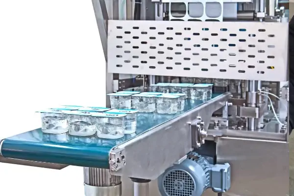 دستگاه ترموفیل سیل اتوماتیک در حال پر کردن و بسته‌بندی ظروف ماست در یک کارخانه