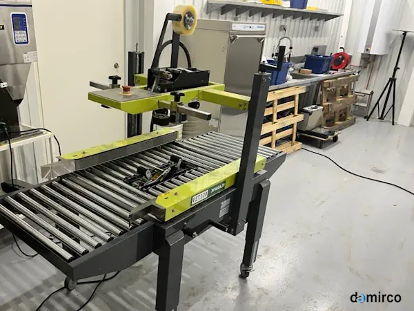 دستگاه چسب زن اتوماتیک در حال چسب زدن کارتن در یک خط بسته بندی صنعتی مدرن