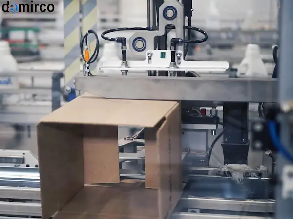 نمای نزدیک از مکانیزم و هد چسب زن دستگاه چسب زن کارتن در حال چسباندن درب یک کارتن قهوه‌ای.