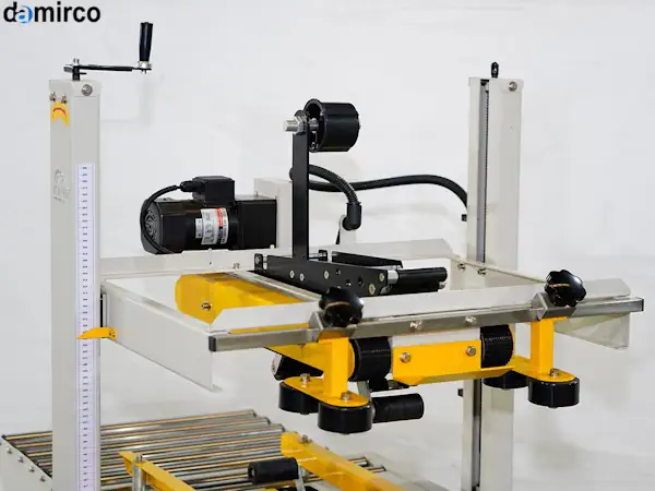 یک دستگاه چسب زن کارتن اتوماتیک در حال چسب زدن درب بالا و پایین یک کارتن قهوه‌ای در یک خط تولید صنعتی.