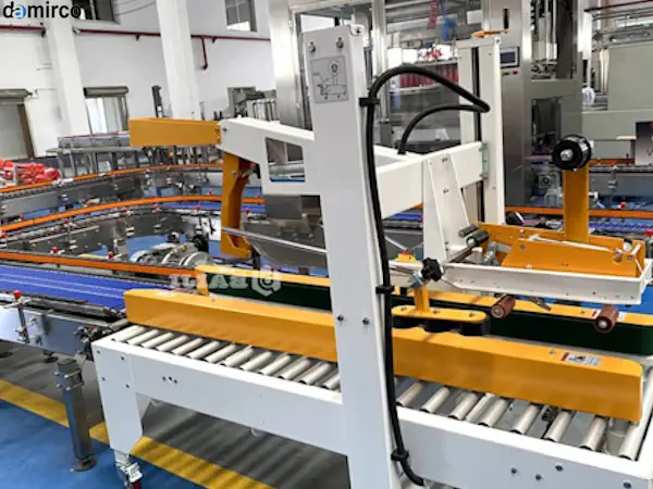 یک دستگاه چسب زن بالا و پایین صنعتی در حال چسب زدن همزمان درب بالا و پایین یک کارتن قهوه‌ای در یک کارخانه