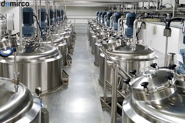 یک میکسر مایعات صنعتی استیل ضد زنگ در حال هم زدن مایعی آبی رنگ در یک مخزن بزرگ