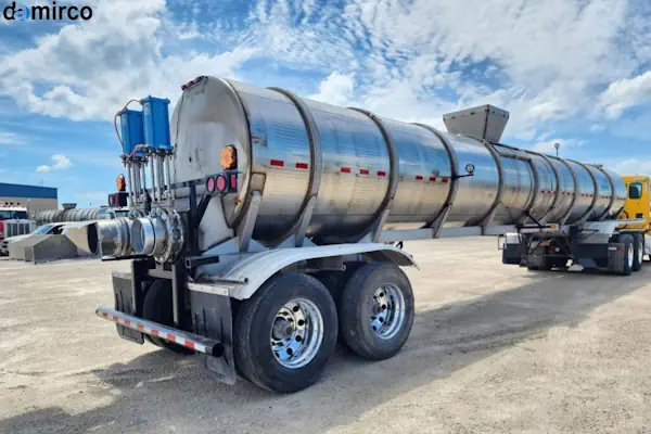 تصویر یک تریلی حمل شیر سفید و براق با مخزن استیل در حال حرکت در جاده