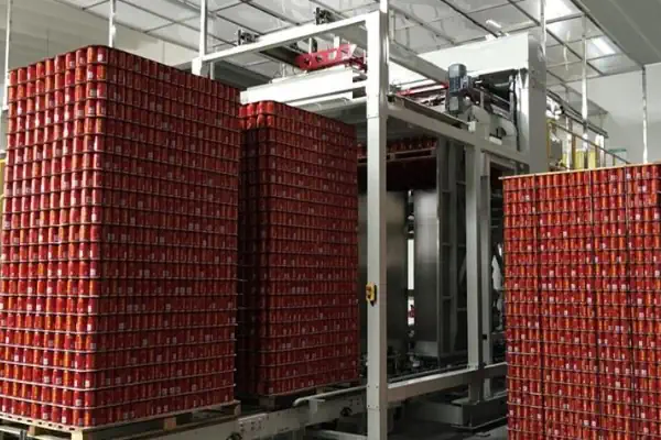 یک دستگاه پالتایزر رباتیک مدرن در حال چیدن منظم کارتن‌ها روی پالت در یک کارخانه صنعتی