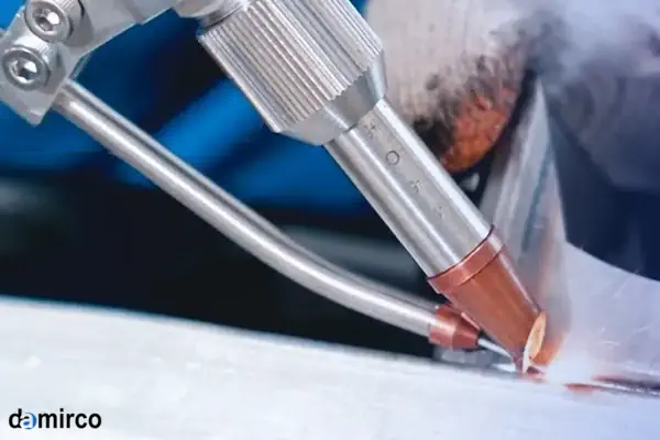 نمای نزدیک از نازل یک دستگاه جوش لیزر در حال کار بر روی قطعه فلزی