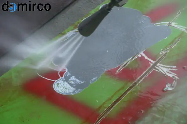 یک دستگاه زنگ زدای واترجت فشار قوی در حال پاک کردن زنگ از روی یک سطح فلزی بزرگ صنعتی.