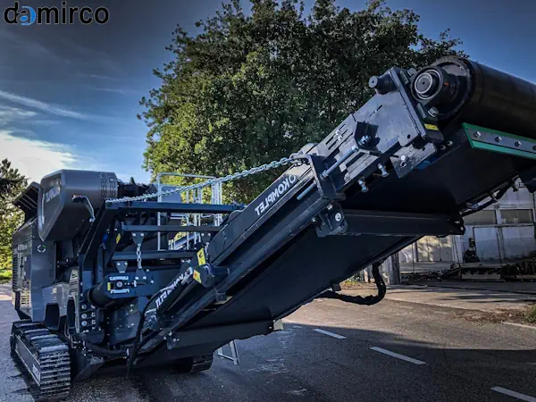 اپراتور مجهز به تجهیزات حفاظت فردی در حال کار ایمن با دستگاه سنگ شکن صنعتی.