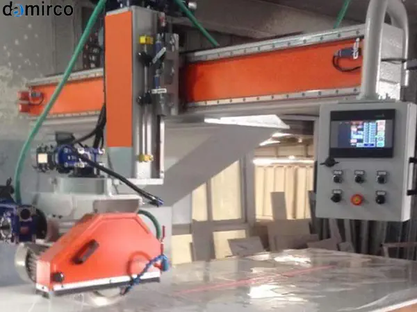 یک دستگاه برش سنگ ساختمانی صنعتی در حال برش یک اسلب سنگ گرانیت با استفاده از آب برای خنک‌سازی تیغه