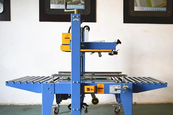 یک دستگاه چسب زن کارتن اتوماتیک در حال بسته‌بندی جعبه‌های مقوایی در یک انبار مدرن.